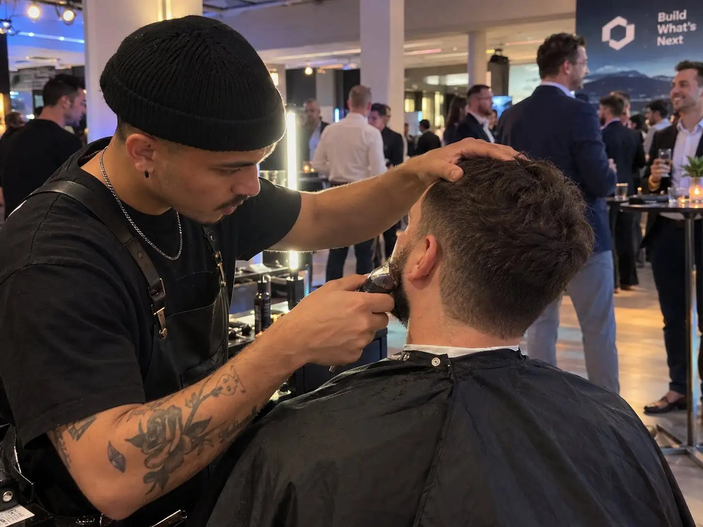 Barber trimmt einem Gast auf einem Firmenevent den Bart, dahinter Networking an Stehtischen – Barber am Messestand