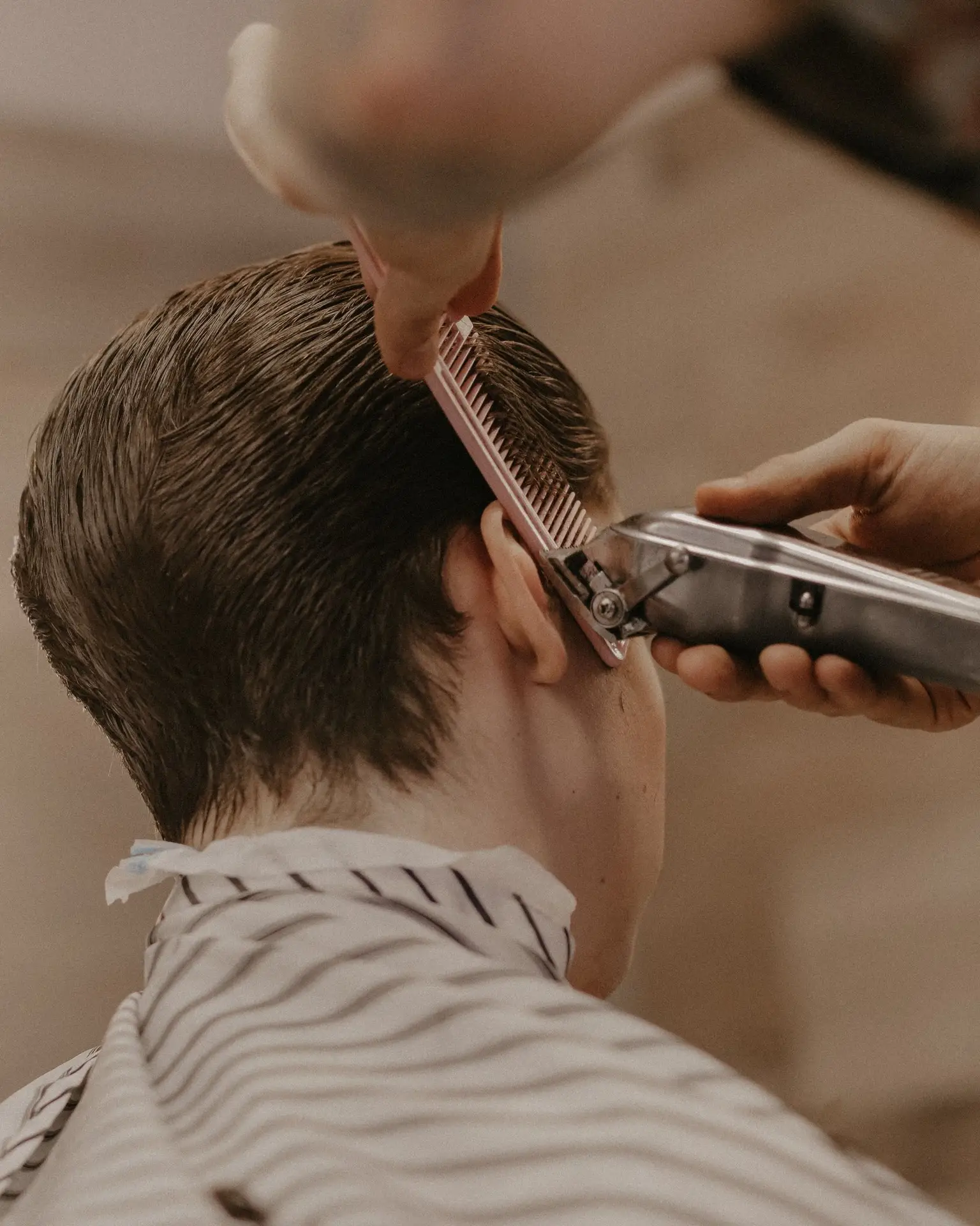 Barber führt die Haarschneidemaschine über dem Kamm und schneidet die Seite über dem Ohr nach – mobiler Friseur in Berlin