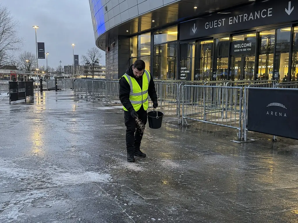 Eventhelfer in Warnweste streut vor dem Gästeeingang einer Arena Salz