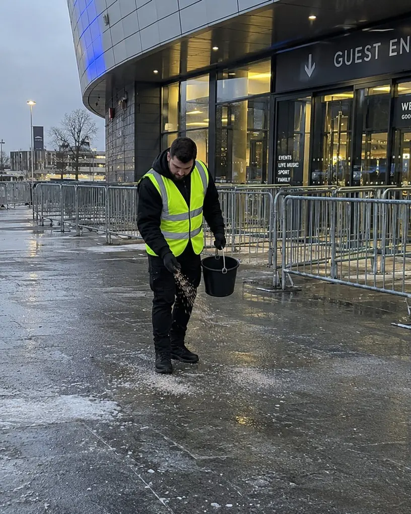 Eventhelfer in Warnweste streut vor dem Gästeeingang einer Arena Salz auf den vereisten Vorplatz – Eventhelfer in Berlin