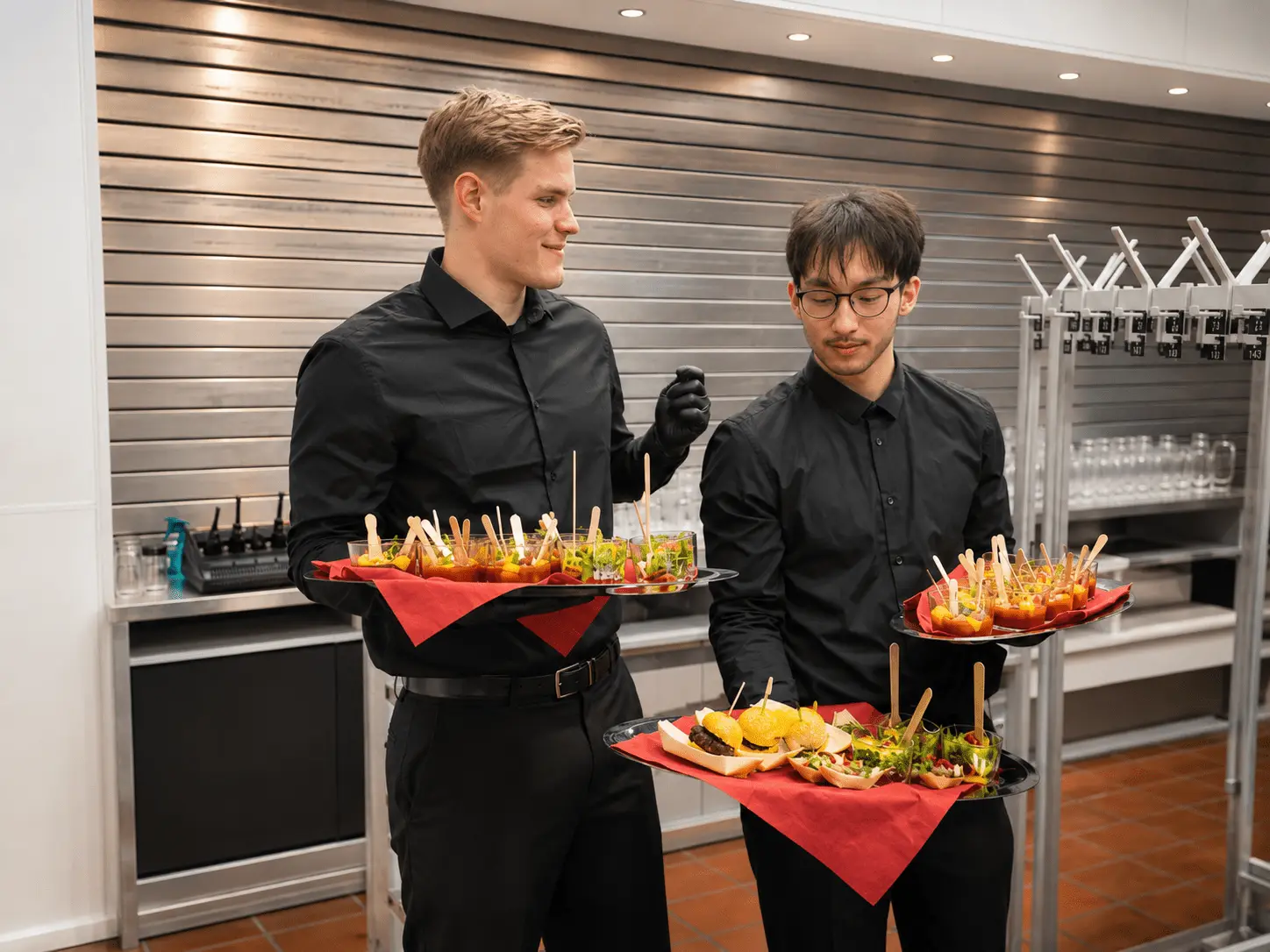 Zwei Servicekräfte in Schwarz tragen Flying-Food-Tabletts mit Häppchen