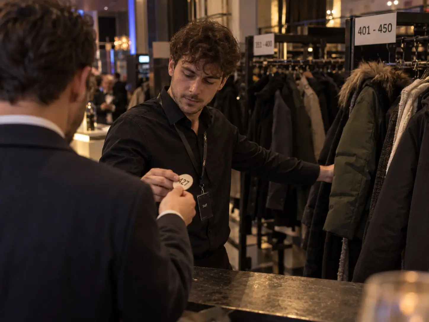 Garderobenkraft reicht einem Gast am Ende der Abendveranstaltung die Garderobenmarke 427 zurück – Garderobenservice in Berlin