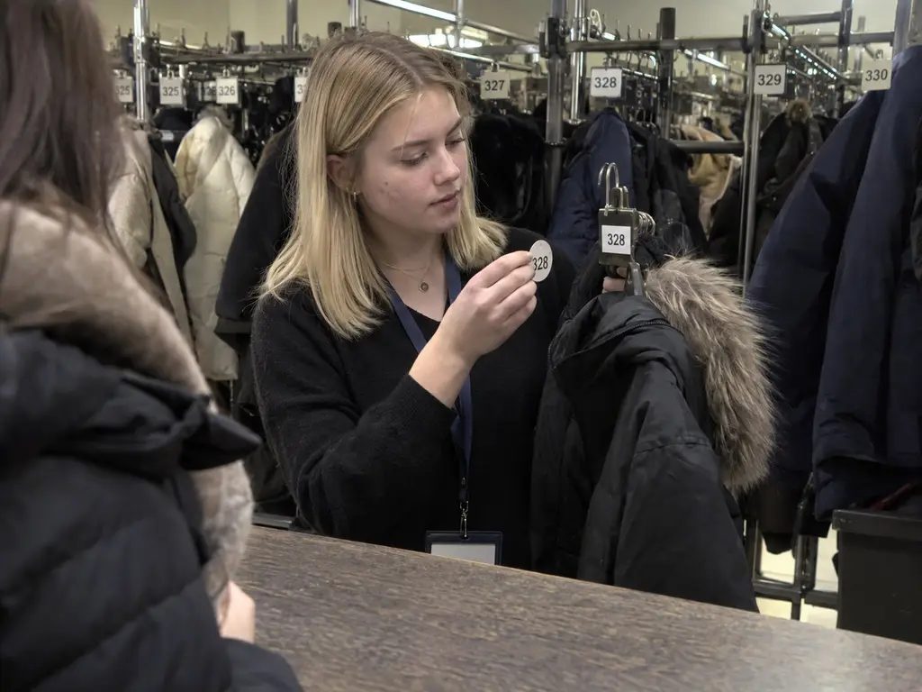 Garderobiere nimmt an einer Abendveranstaltung eine Winterjacke entgegen und gibt die Garderobenmarke aus