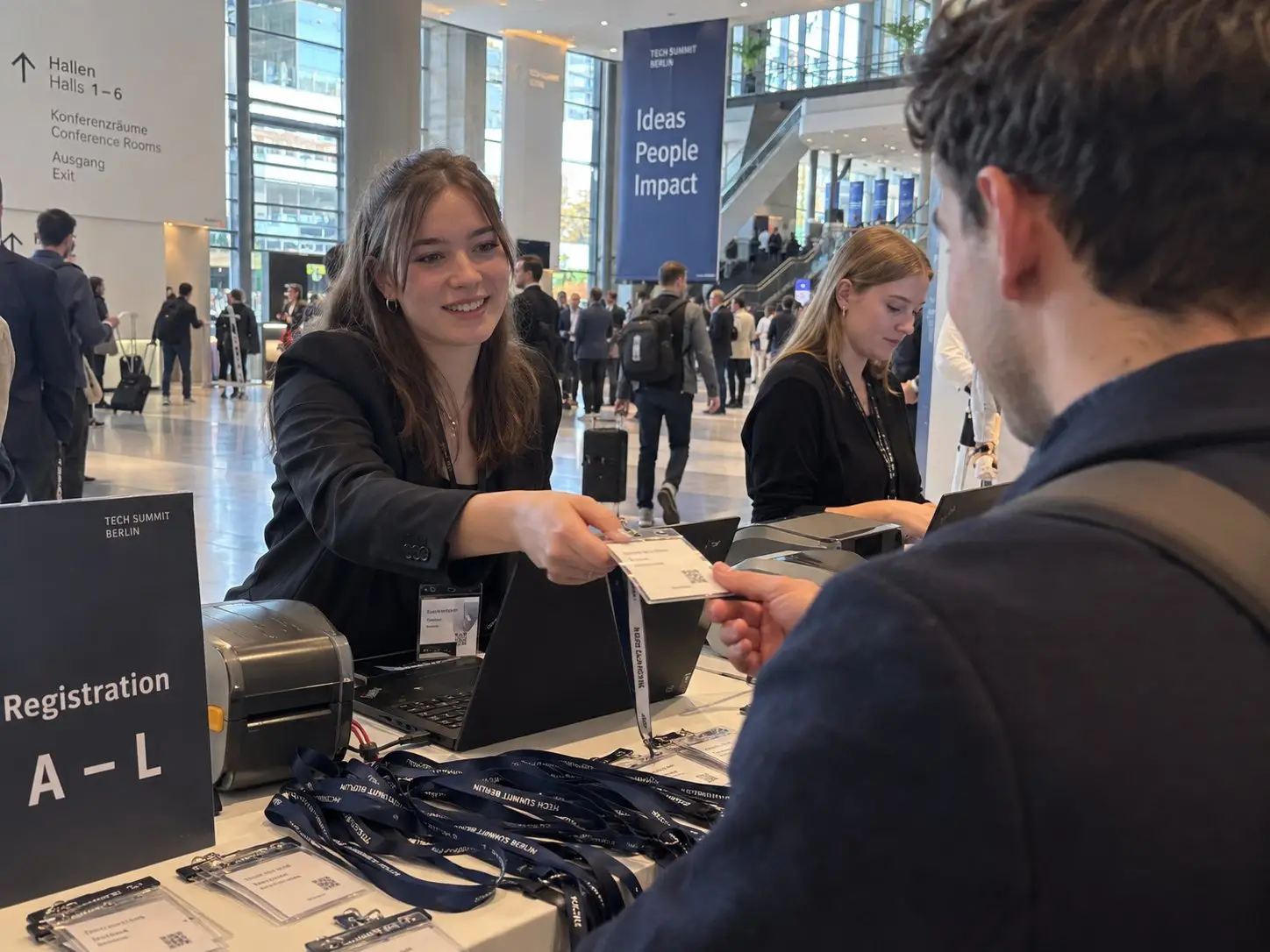Hostess reicht an der Registrierung einer Tech-Konferenz einem Teilnehmer sein Namensschild mit Lanyard – Akkreditierungspersonal in Berlin