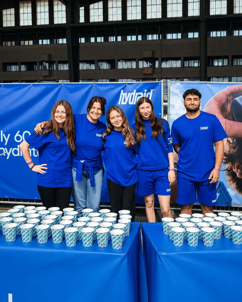 Promotionteam in blauen Markenshirts hinter Sampling-Tresen mit Bechern