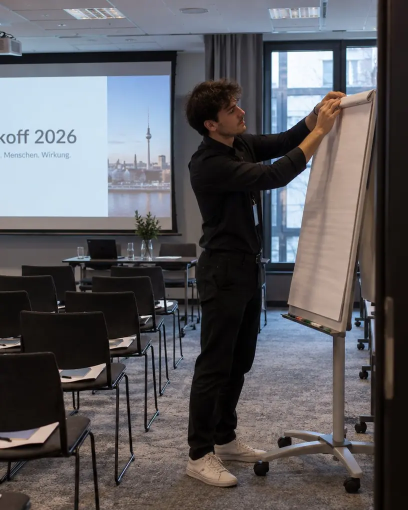 Servicekraft bereitet im Workshop-Raum einer Kick-off-Tagung das Flipchart vor, im Hintergrund Leinwand und Stuhlreihen – Personal für den Neujahrsempfang