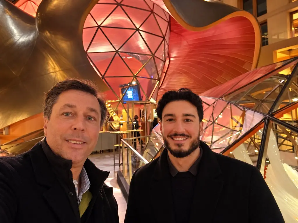 Selfie of Leon Chiosea (right) and a business partner in front of curved, red-lit architecture