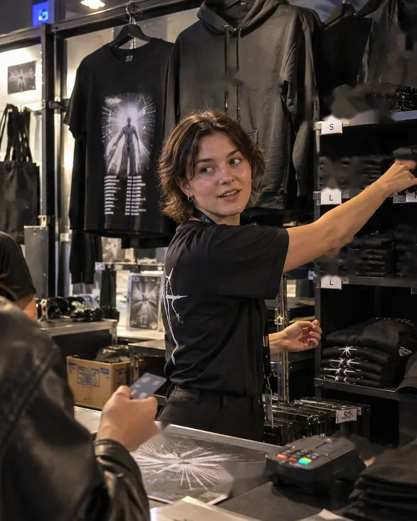 Sales assistant at a merchandise stand takes a T-shirt from the shelf while a customer holds her card