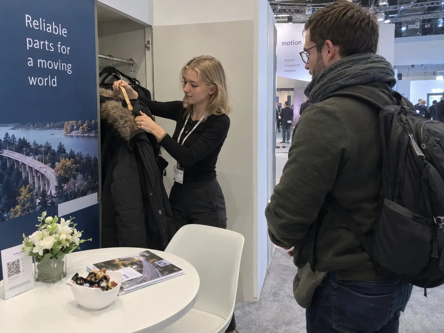 Stand hostess hangs up a visitor’s coat at a trade fair stand