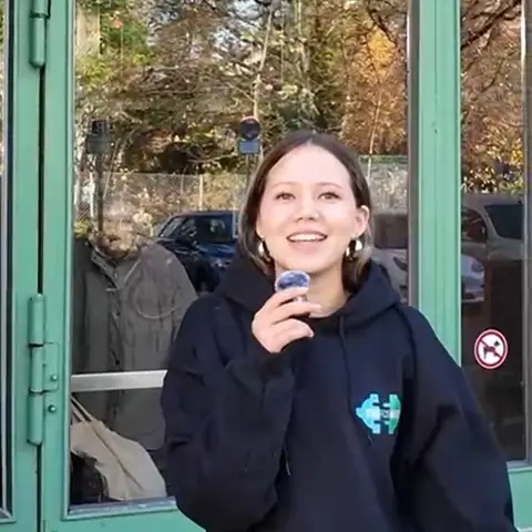 A StaffConnect team member in a hoodie holds a clip-on microphone in front of a green glass door