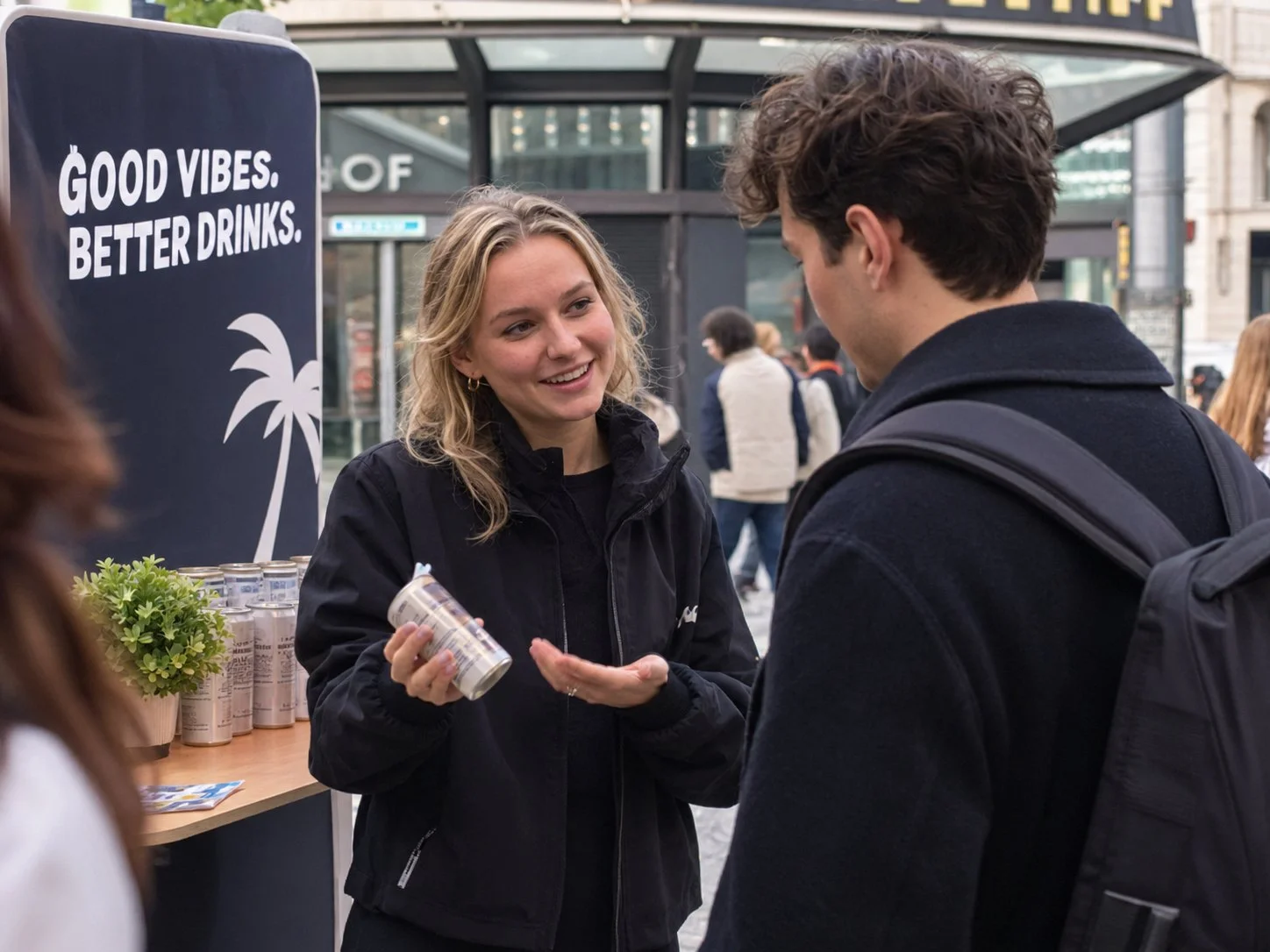 Promoterin erklärt einem Passanten an einem Aktionsstand ein Getränk