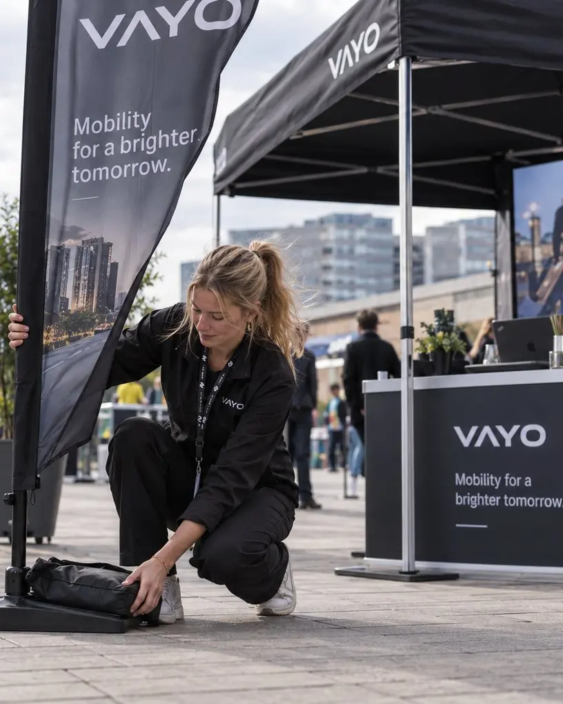Promoterin richtet vor ihrem Aktionsstand eine Beachflag aus, im Hintergrund der Berliner Fernsehturm – Promotionpersonal in Berlin
