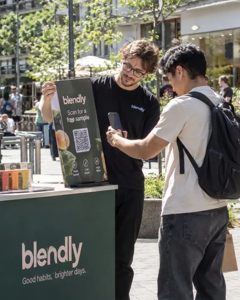 Promoter shows a passer-by the QR code for a free sample at a sampling stand