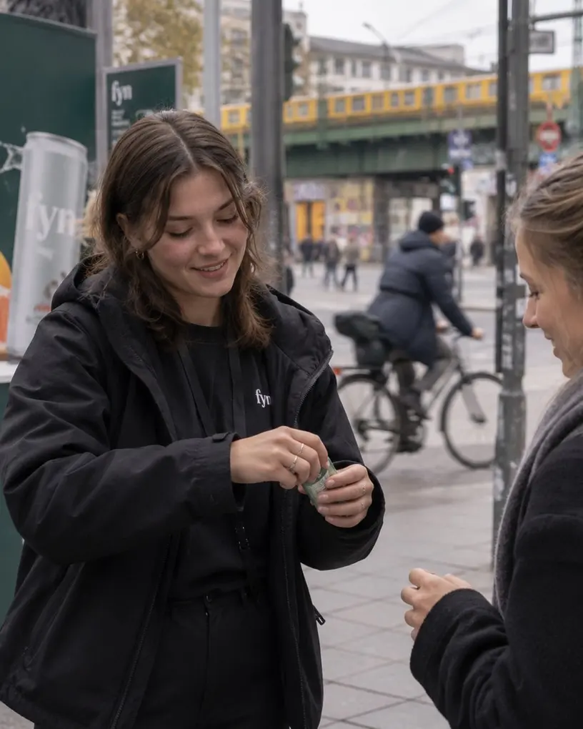 Promoter in a winter coat hands a product sample to a passer-by on a Berlin street