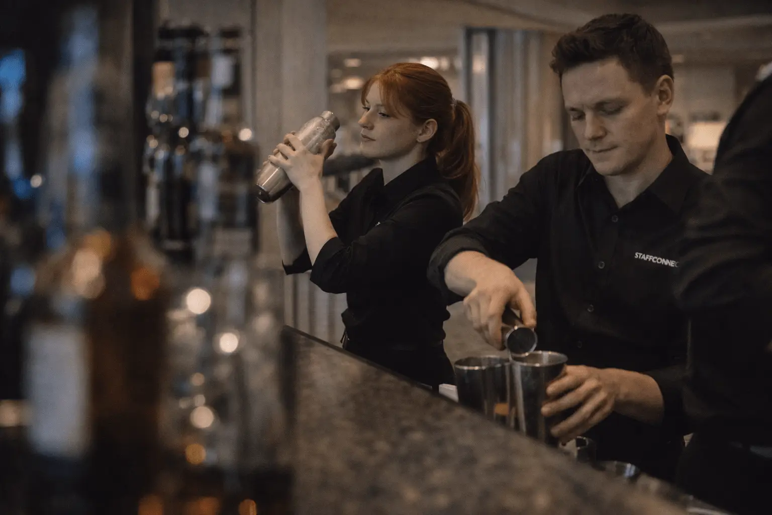 Zwei Barkeeper mixen Cocktails mit Shakern hinter einer Bar