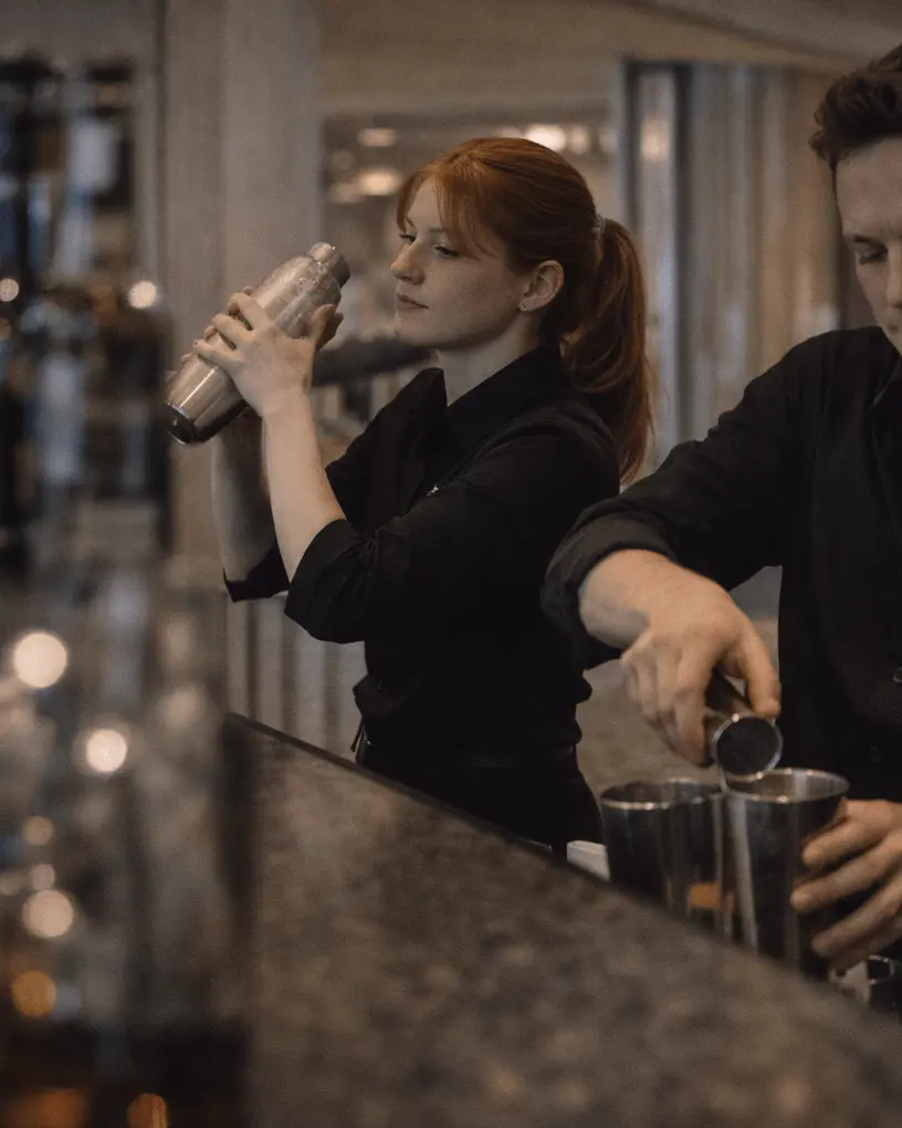 Two bartenders in black mixing drinks behind a hotel bar